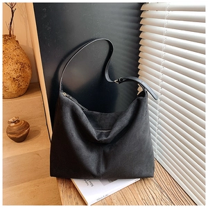 Détail d'un sac hobo en daim noir avec couture centrale sur une surface en bois