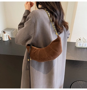 Detail of dark brown suede croissant bag with woven chain strap worn by a model