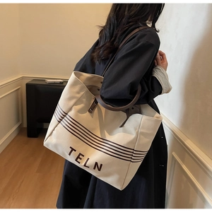 Detail of canvas tote bag with leather handles and striped pattern worn on shoulder
