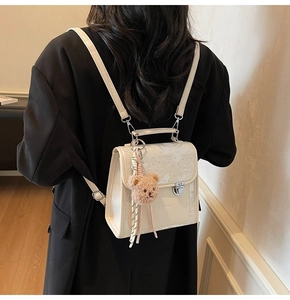 Detail of white PU leather backpack with floral patterns, metal lock, and bear charm