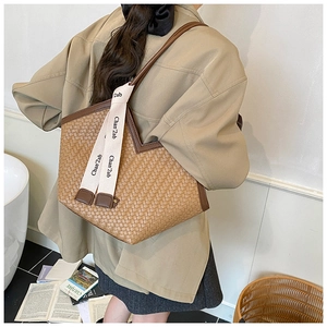 Detail of hand-woven tote bag with leather straps and decorative logo ribbon