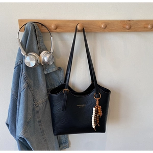 Detail of black faux leather tote bag with gold lettering and colorful bead pendant