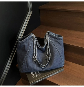 Detail of vintage denim tote bag showing frayed edges and silver chain strap on stairs