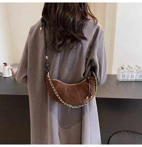 Close-up of brown suede crescent bag with gold chain and knotted leather strap on model