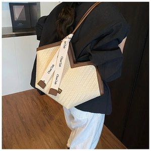 Close-up of woven straw tote bag with brown leather handles and decorative ribbon