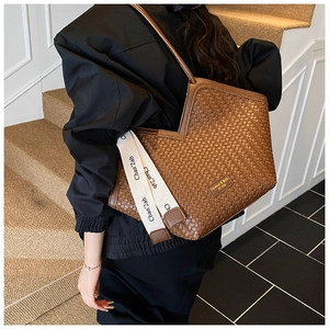 Detail view of woven leather texture and golden logo plate on brown tote bag