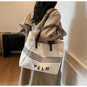 Detail view of canvas tote bag with brown stripes and leather straps worn by a model
