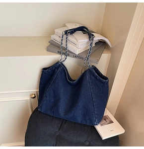 Detailed close-up of dark blue denim tote bag with silver chain and woven fabric shoulder strap