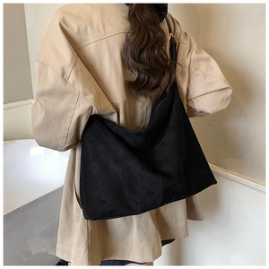 Vue arrière d'un grand sac hobo en daim noir minimaliste porté avec un trench-coat kaki