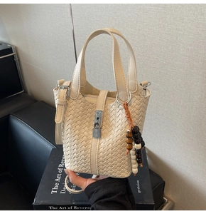 Détail d'un sac seau tressé beige avec fermoir métallique et breloque en perles de bois
