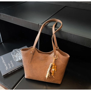 Detail of vintage brown leather tote bag with MIKKO J branding and wooden bead charm