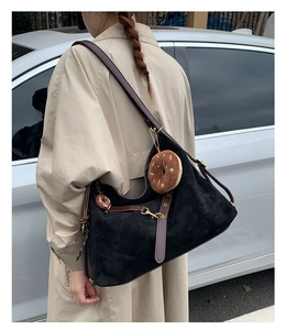 Detail of black suede tote bag with brown leather strap and donut plush charm decoration
