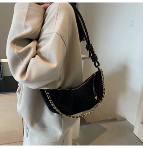 Close-up of black suede dumpling bag with woven gold chain and pleated texture details