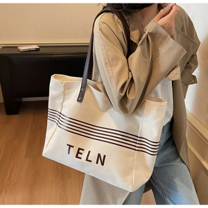 Close-up of a large canvas tote bag with leather handles and TELN logo print detail