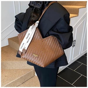 Detail of a brown woven tote bag featuring a V-shaped opening and decorative silk scarf