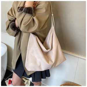 Detail of a large beige suede hobo bag with zip closure and soft texture over the shoulder