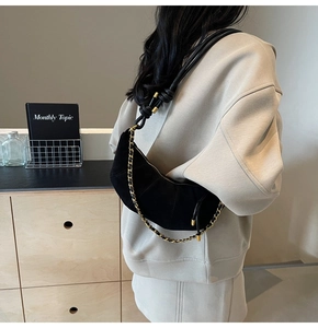 Detail of black suede hobo bag with vintage gold chain and cylindrical strap worn on shoulder