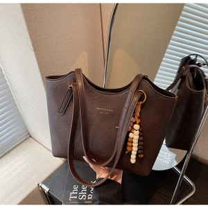 Detailed close-up of dark brown leather tote bag with vintage beaded charm and logo