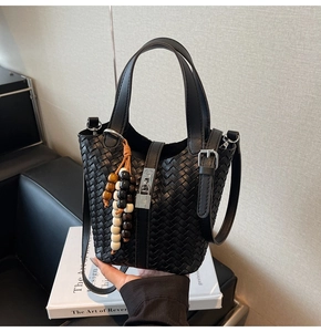 Détail d'un sac seau en cuir tressé noir avec fermoir argenté et breloque perlée