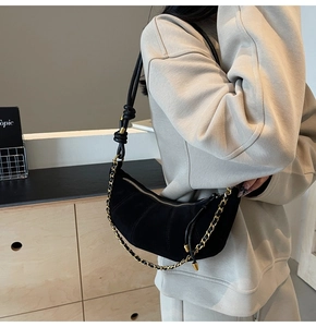 Detail of black suede crescent bag featuring quilted texture and metallic chain strap