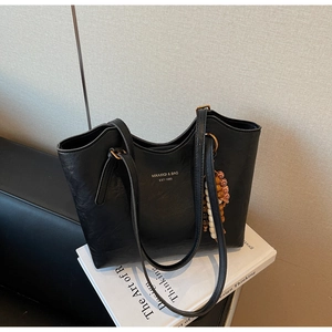 Close-up of black PU leather tote bag with wooden bead tassel and printed logo