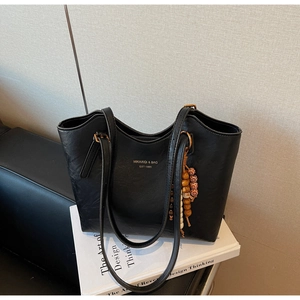 Detail of black leather tote bag with brand lettering and vintage wooden bead tassel