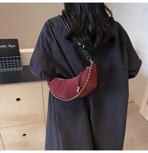 Detail of burgundy suede croissant bag with chain strap in elegant indoor setting