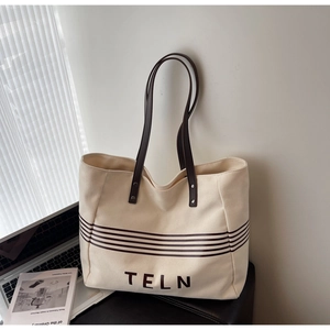 Detailed macro view of beige canvas tote bag with brown leather handles and TELN logo