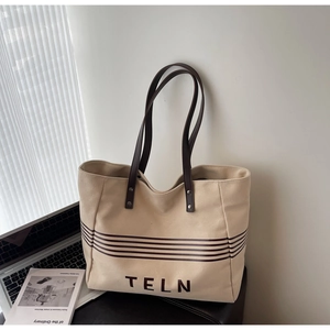 Canvas tote bag with TELN lettering and brown leather handles in a cozy home office setting