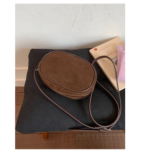 Close-up of brown suede oval crossbody bag featuring premium leather trim and metal zipper