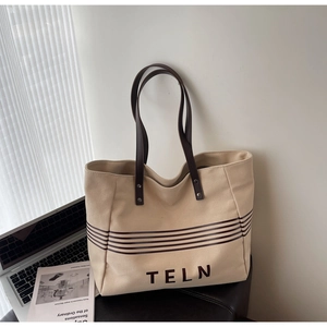 Close-up of a large canvas tote bag with dark stripes and brown leather handles