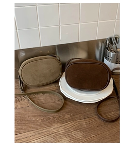 Close-up of olive green and brown suede crossbody bags on a wooden table with tiles