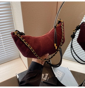 Detail of burgundy suede croissant bag with quilted folds and golden chain strap