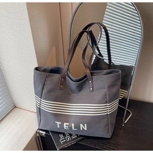 Detail of dark grey canvas tote bag with brown leather handles and striped TELN design