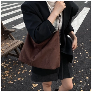 Détail d'un sac hobo en daim marron foncé avec pompon dans un décor de rue urbain
