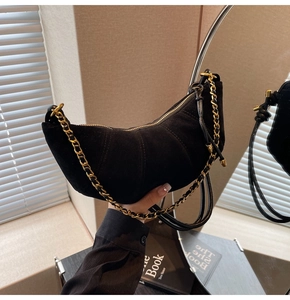 Detail of black matte croissant bag featuring gold chain and textured curved stitching