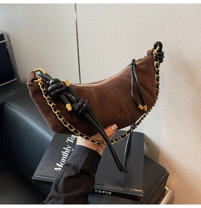 Close-up of brown suede croissant bag with black leather knots and gold chain strap