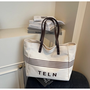 Close-up of canvas tote bag with brown stripes, leather handles, and TELN logo detail
