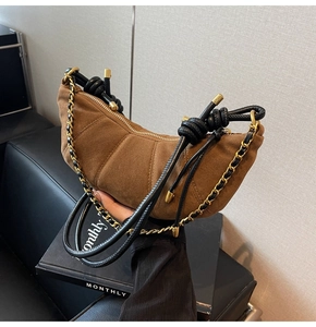 Detail of a brown suede croissant bag with black drawstring and gold metal chain strap