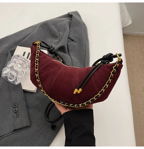 Detail of burgundy suede dumpling bag with gold chain strap and tassel zipper puller