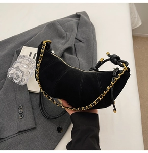 Detail of matte black leather crescent bag featuring gold chain and knotted leather strap