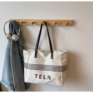 Detail of canvas tote bag with TELN logo, brown leather handles and metal rivet reinforcement