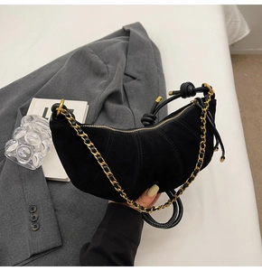Detail of black matte suede dumpling bag with vertical quilting and gold chain strap