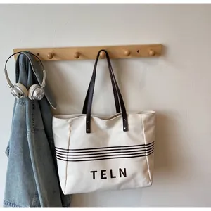 Detail of canvas tote bag showing the leather handles and striped TELN brand design