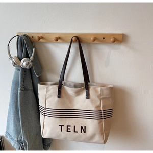 Detail of canvas tote bag with brown straps and TELN logo on a lifestyle background