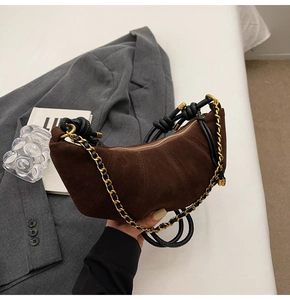 Close-up of brown suede croissant bag with woven gold chain strap and pleated detail