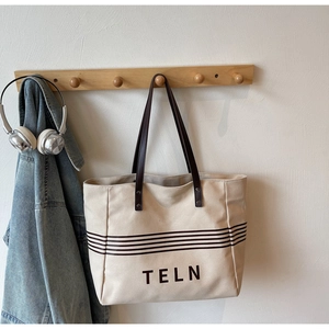 Detail of canvas tote bag with brown leather handles and striped print hanging on a hook