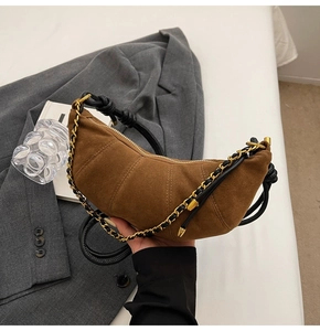Close-up of brown suede crescent bag with segmented stitching and gold chain strap