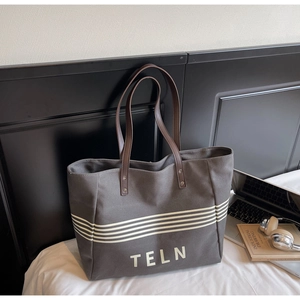 Detail of grey canvas tote bag with brown leather handles and TELN letter printing