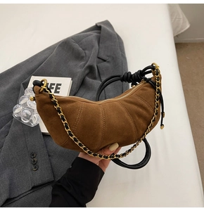 Detail of a brown suede croissant bag featuring a gold chain and leather knot strap